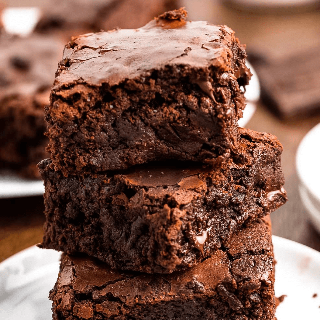 Stack of three chocolate brownies on a white plate.
