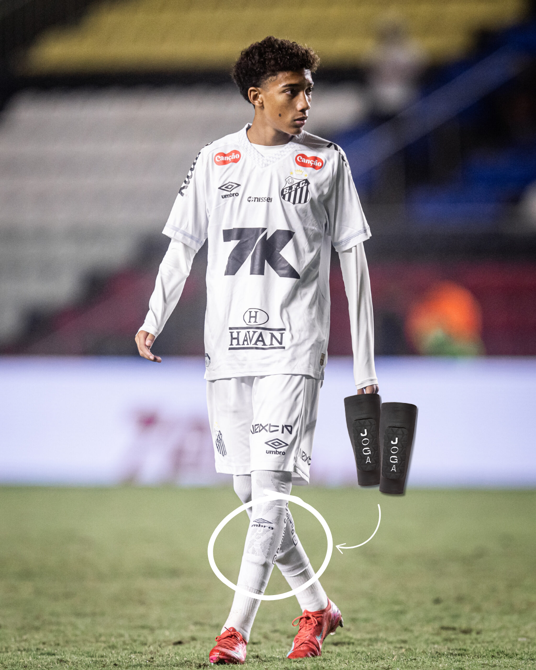 Soccer player in white uniform on field, holding black shin guards.
