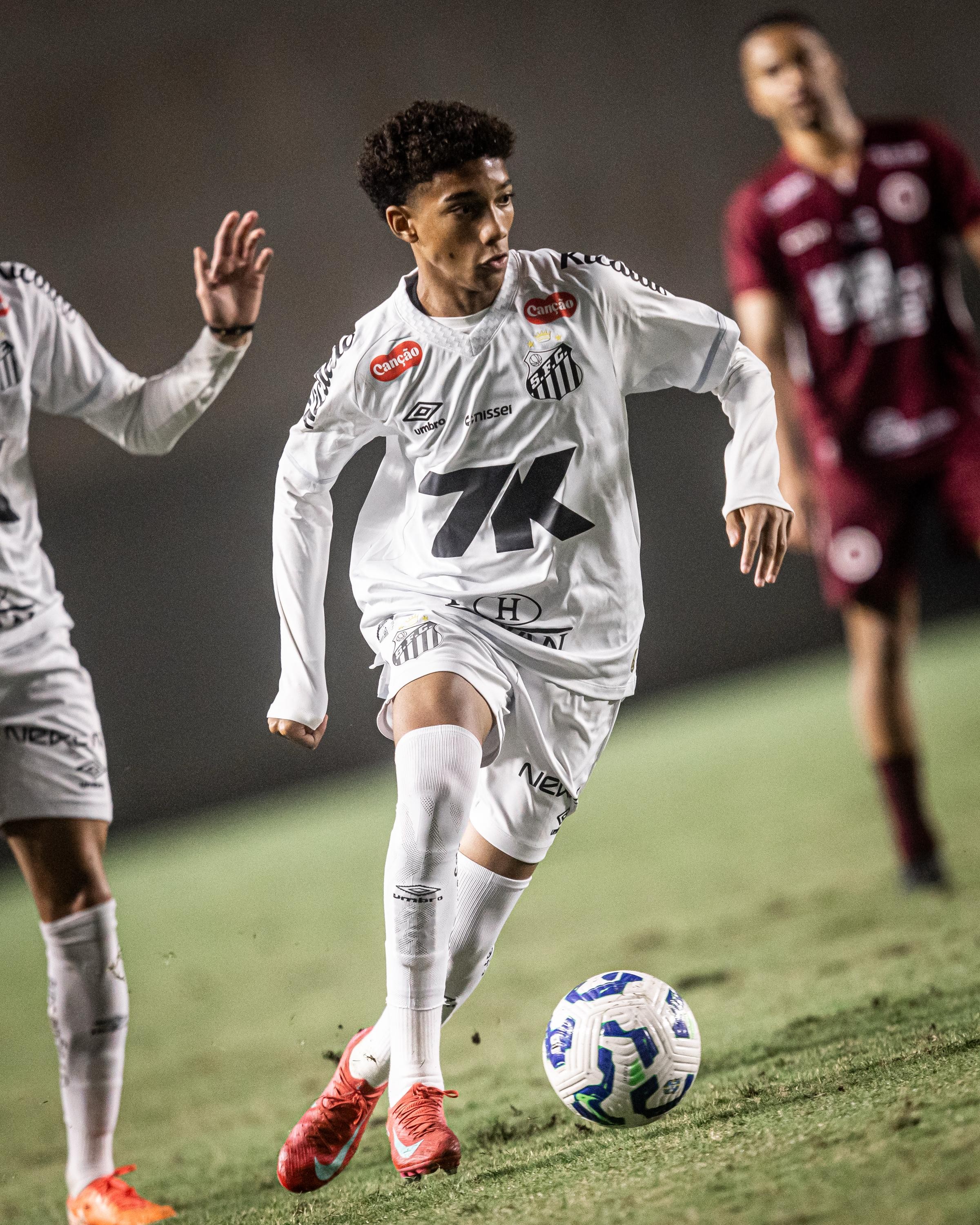 Soccer player in white uniform dribbling a ball on a field during a match.