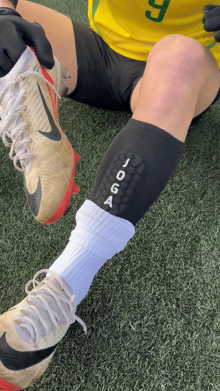 Person wearing soccer gear, showing shin guard and cleats on grass field.