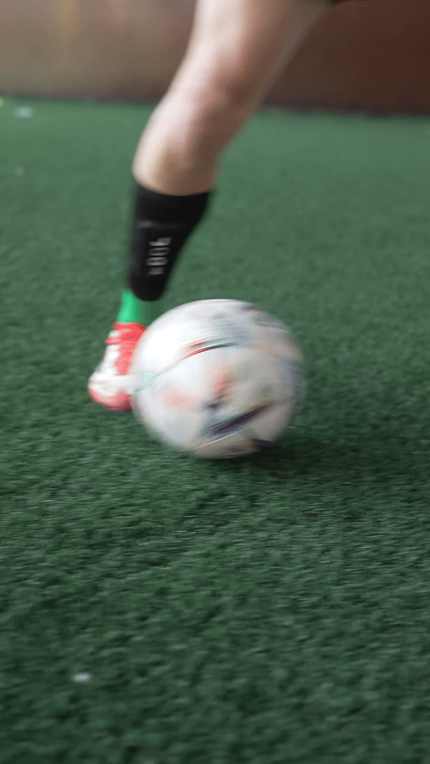 Person kicking a soccer ball on green turf.