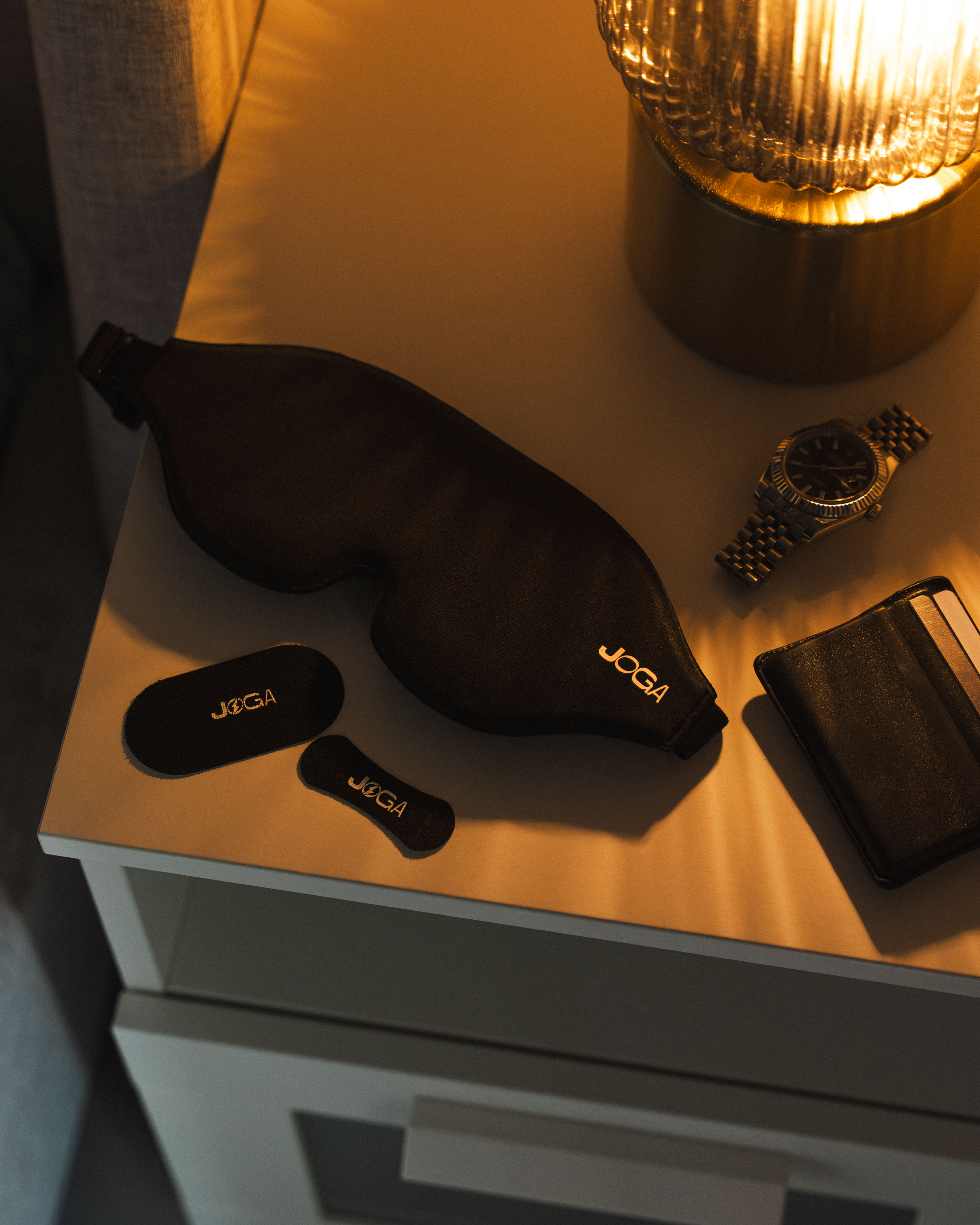Nightstand with sleep mask, watch, wallet, and lamp.