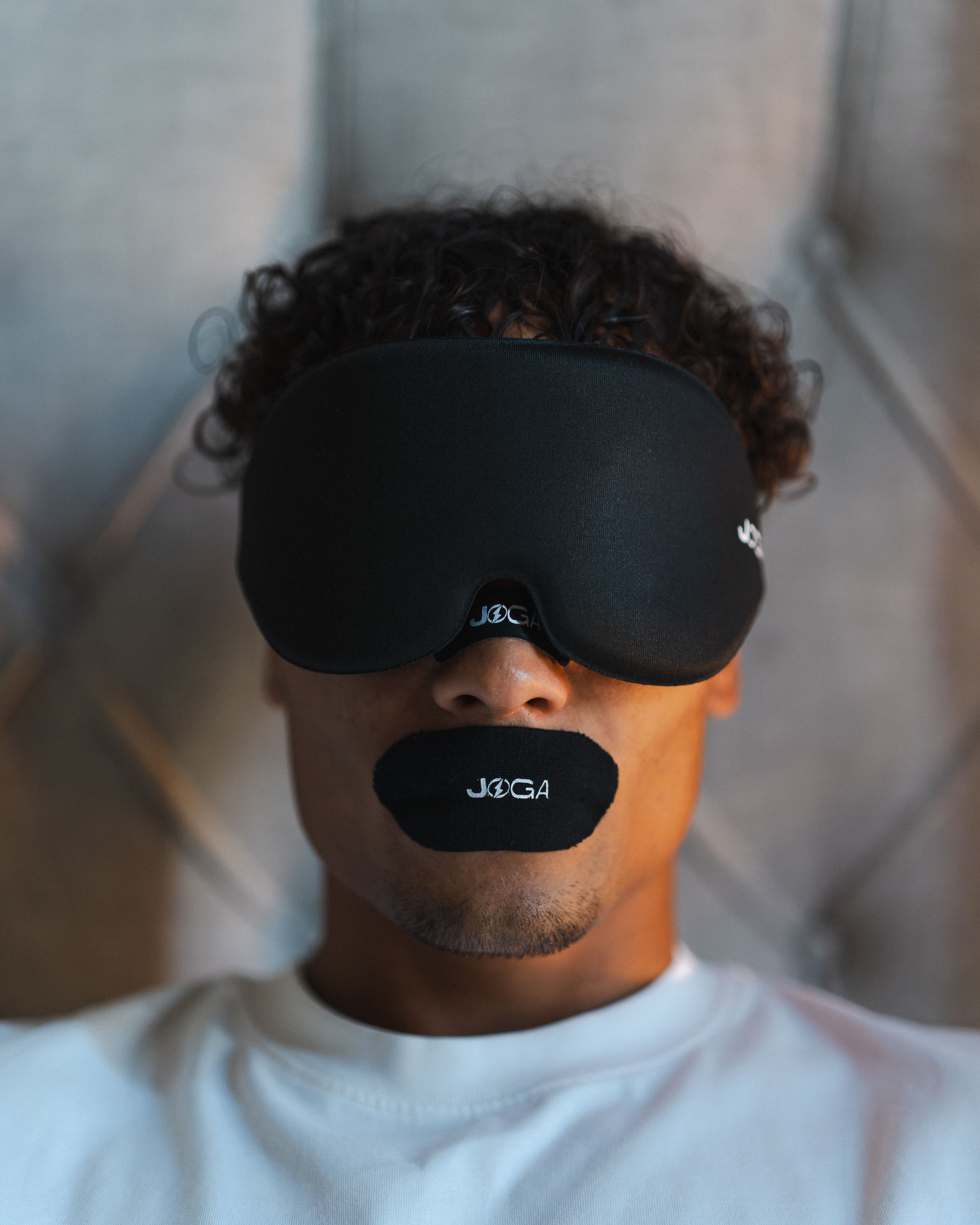 Person wearing a black sleep mask and mouth cover with 'JOGA' logo.