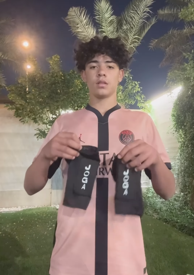 Person holding two black socks with 'JOGA' text, standing outdoors at night.