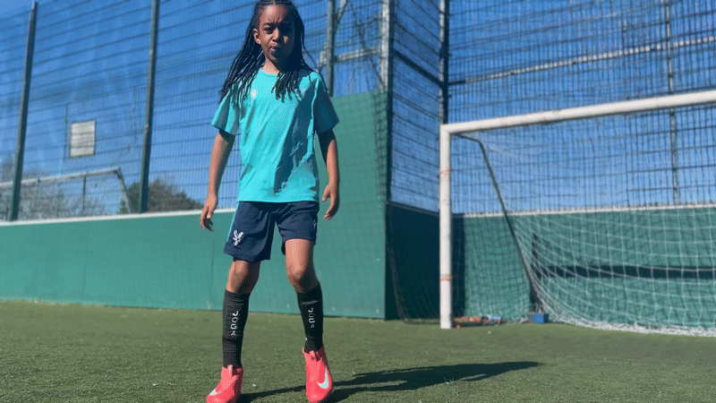Child in sportswear standing on a soccer field near a goal.