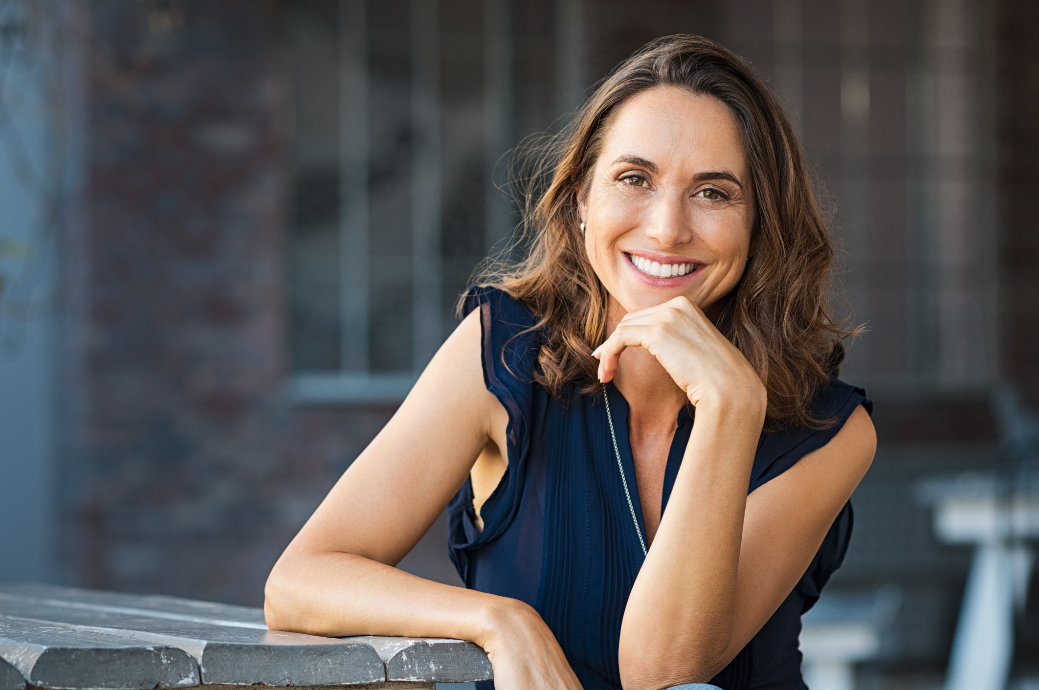 Smiling woman sitting at a table outdoors.