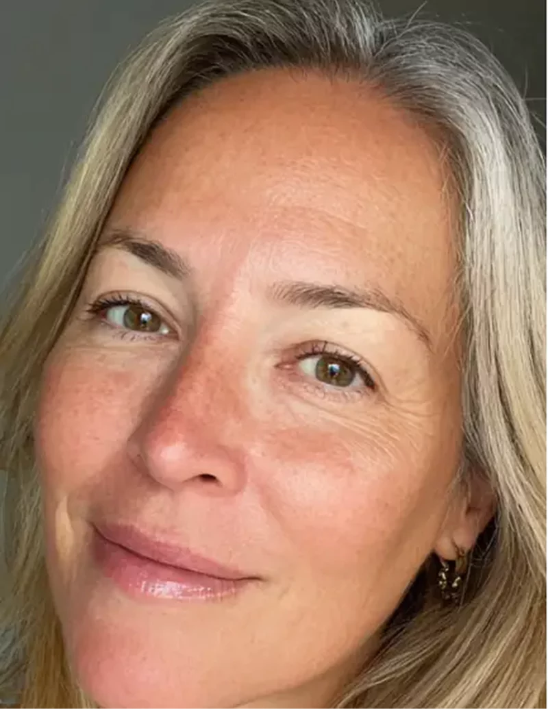 Close-up of a smiling person with light hair and earrings.