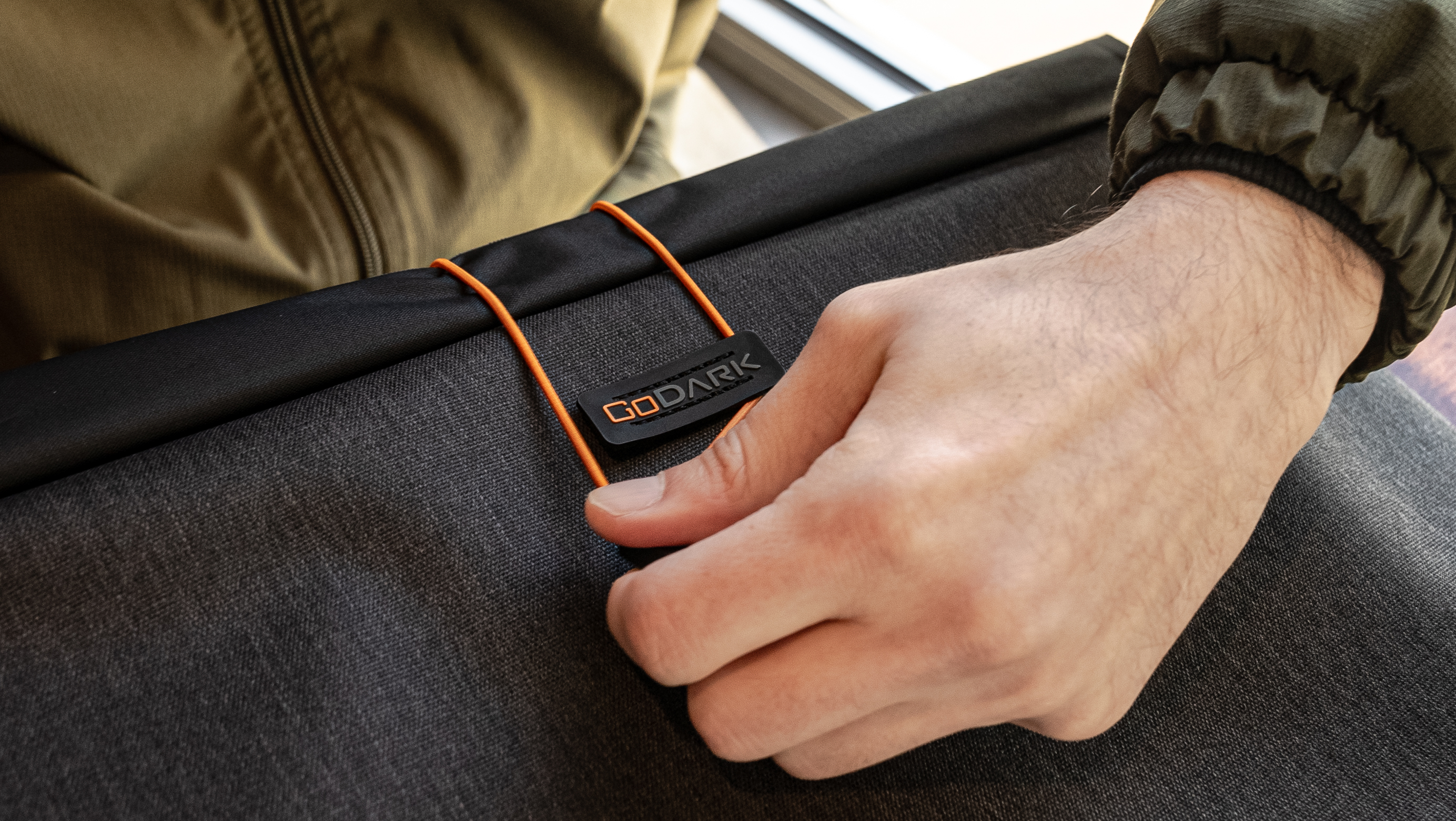 Hand holding a black fabric with orange cords and a 'GoDark' label.