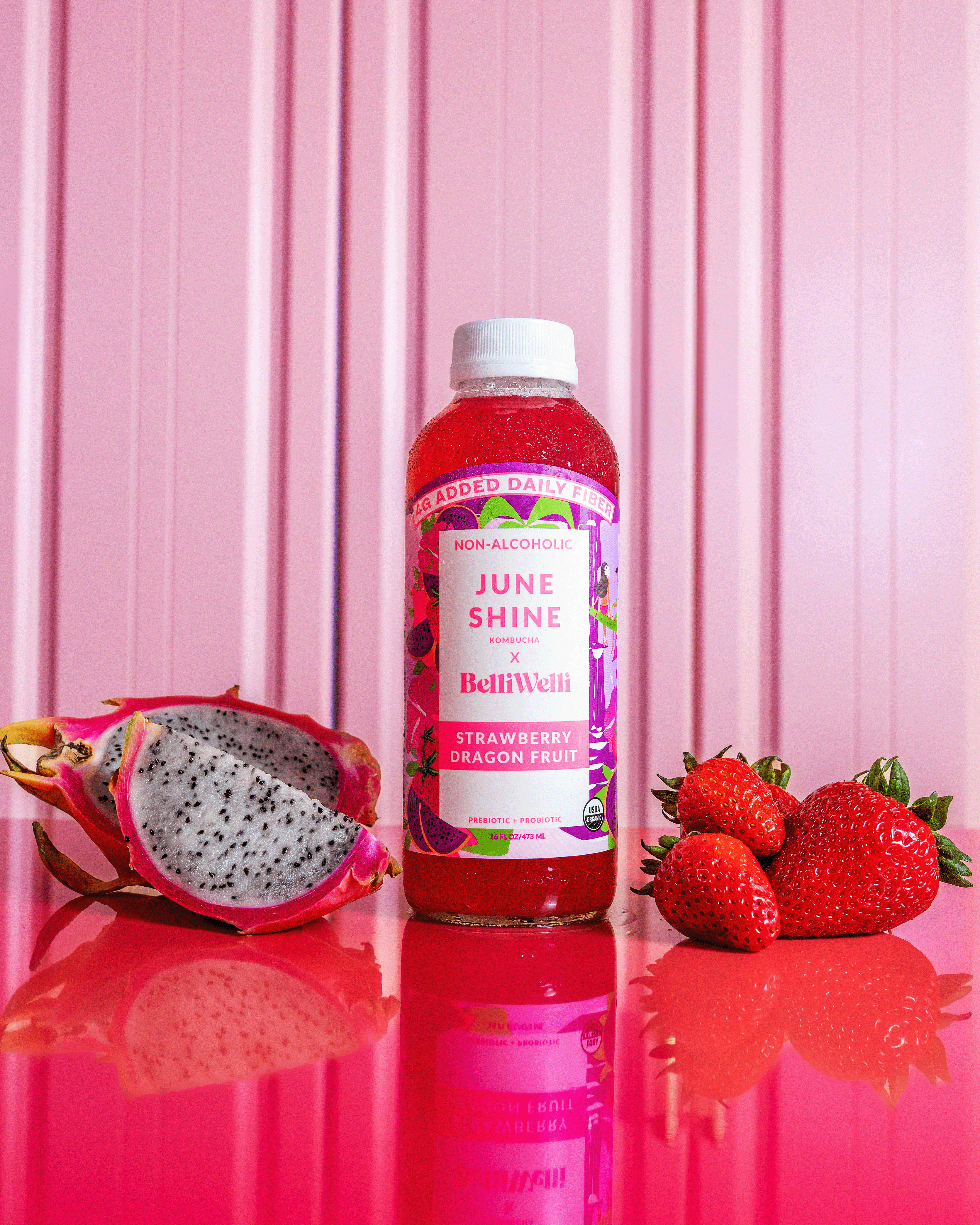 Bottle of June Shine kombucha with strawberries and dragon fruit on a pink background.
