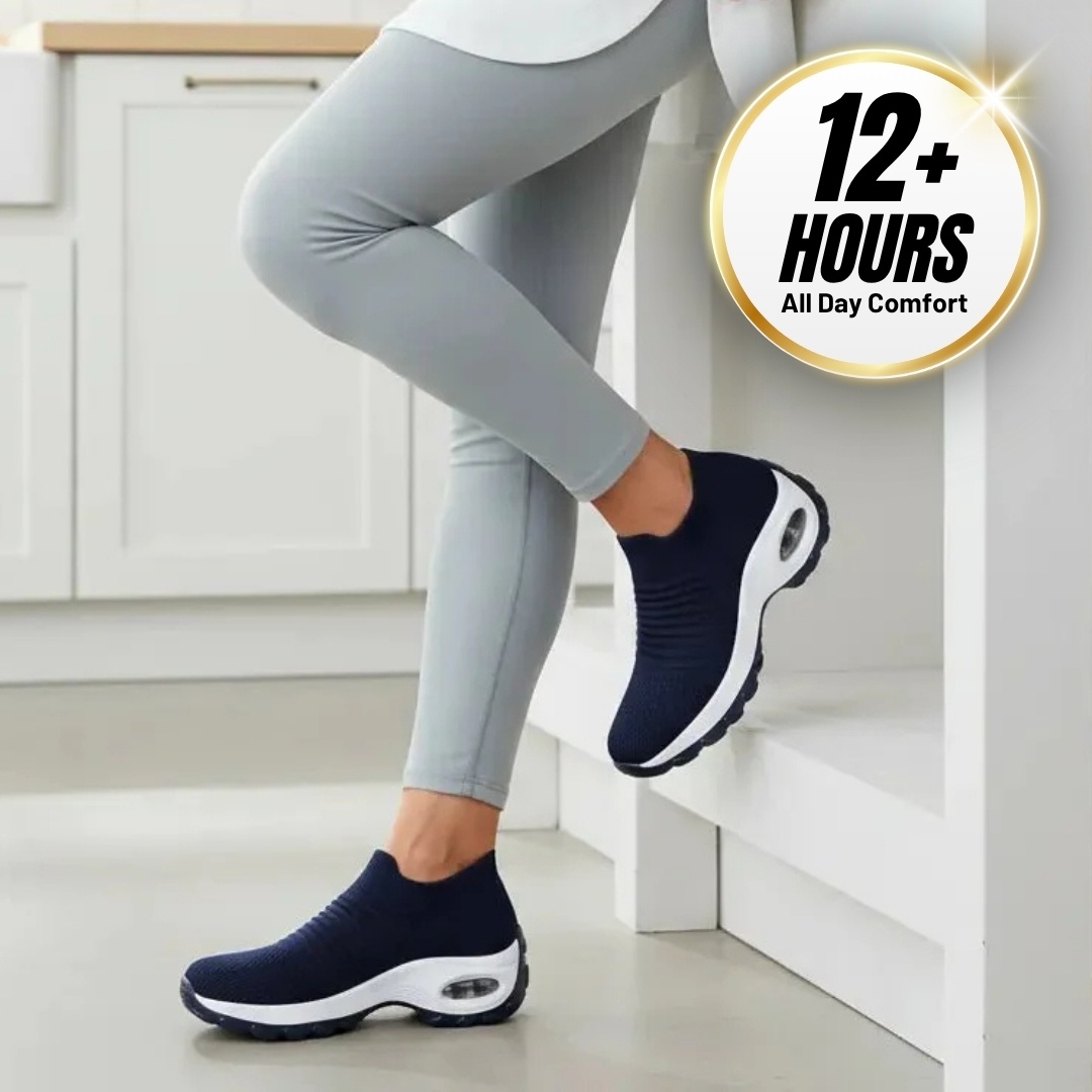 Person wearing navy slip-on sneakers and gray leggings, leaning against a white wall.