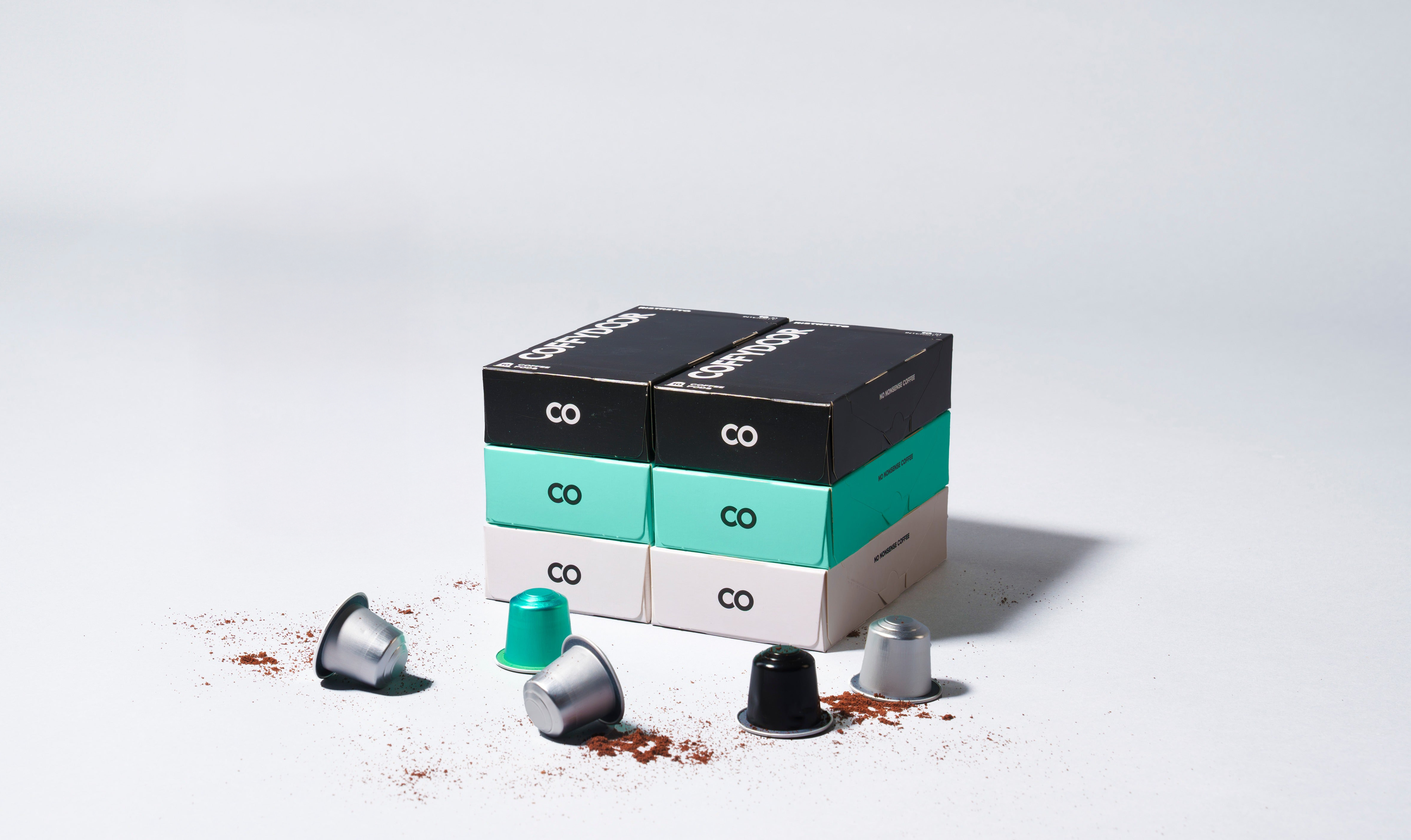 Stacked coffee pod boxes with scattered coffee pods and grounds.