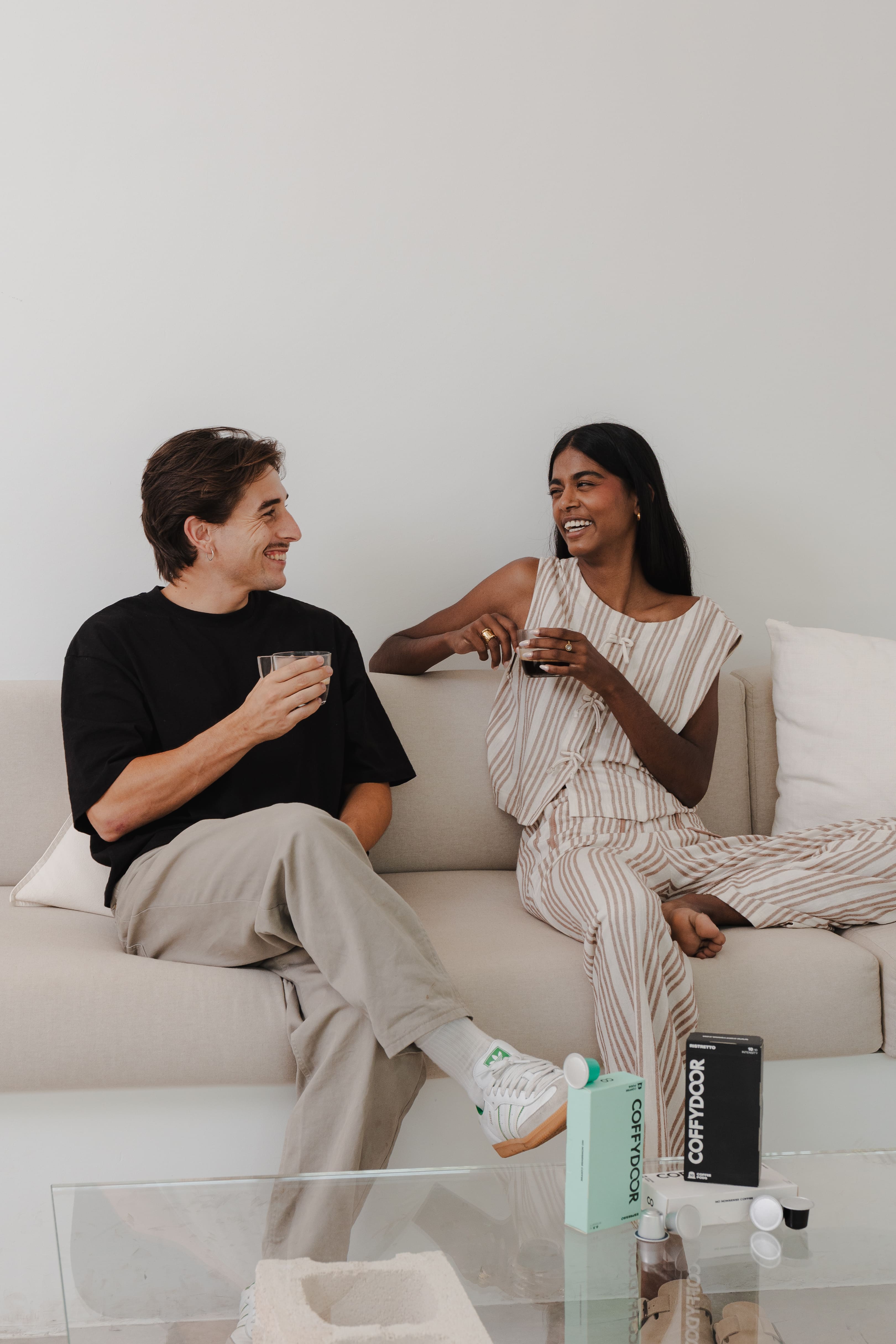 Two people sitting on a couch, smiling and holding drinks.