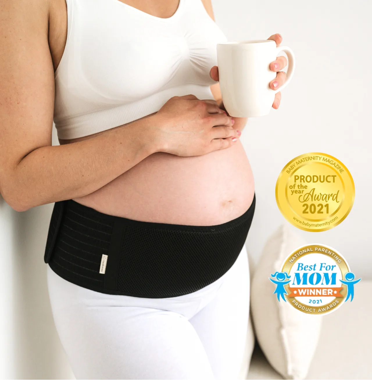 Pregnant person holding a mug, wearing a support belt, with award badges displayed.