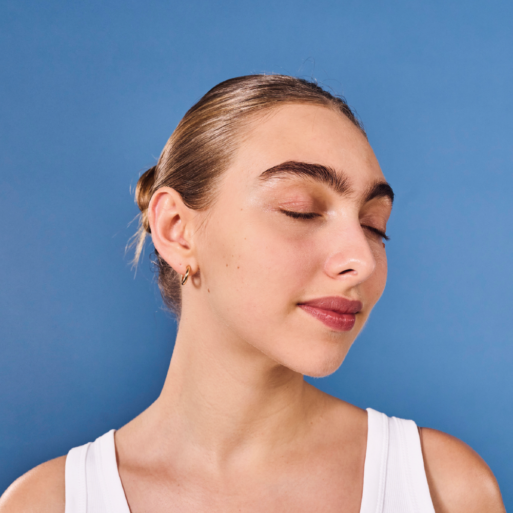 A woman with her hair pulled back and eyes closed smiles serenely against a solid blue background.
