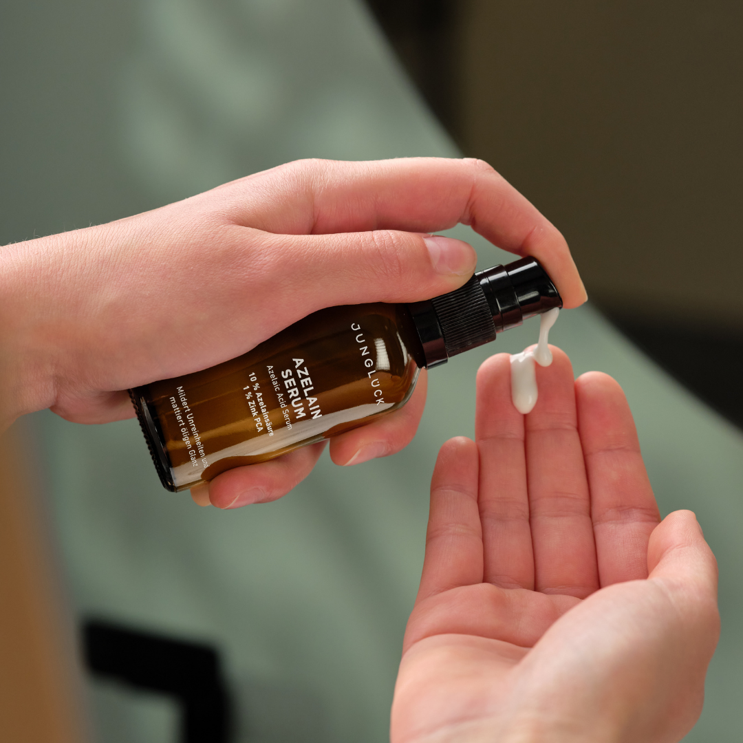 A person pumps white serum from a brown glass bottle onto their fingers.