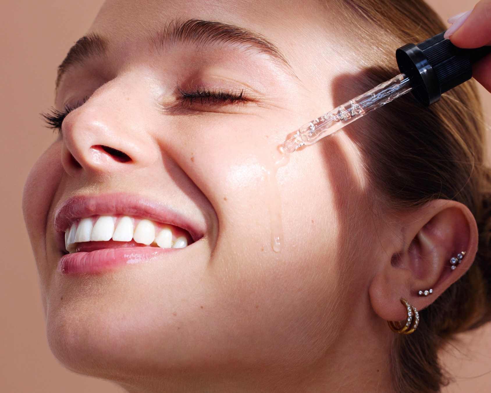 Close-up of a smiling person applying serum with a dropper on their face.