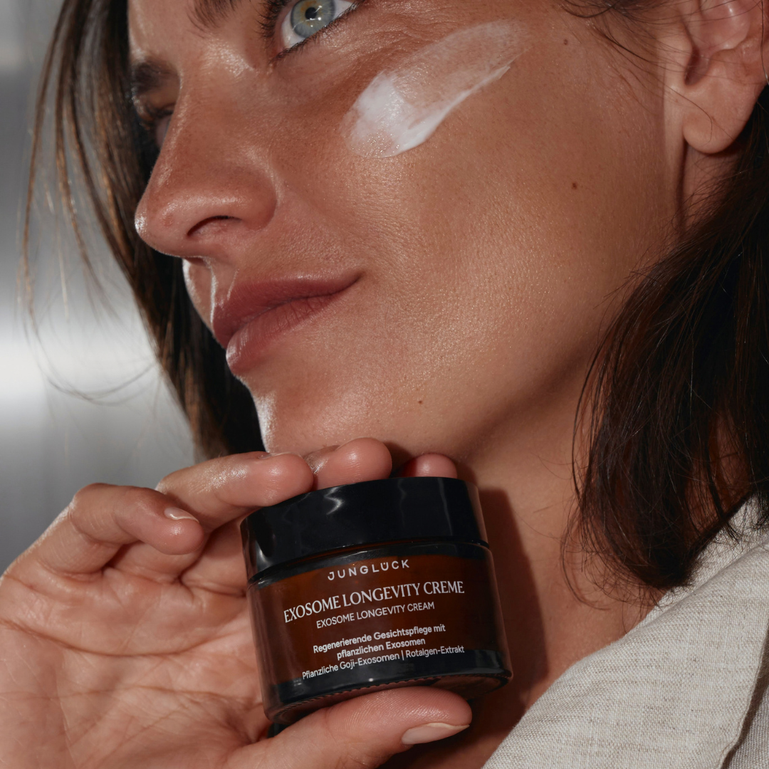 A woman with a swipe of cream on her cheek holds a jar of Junglück face cream.