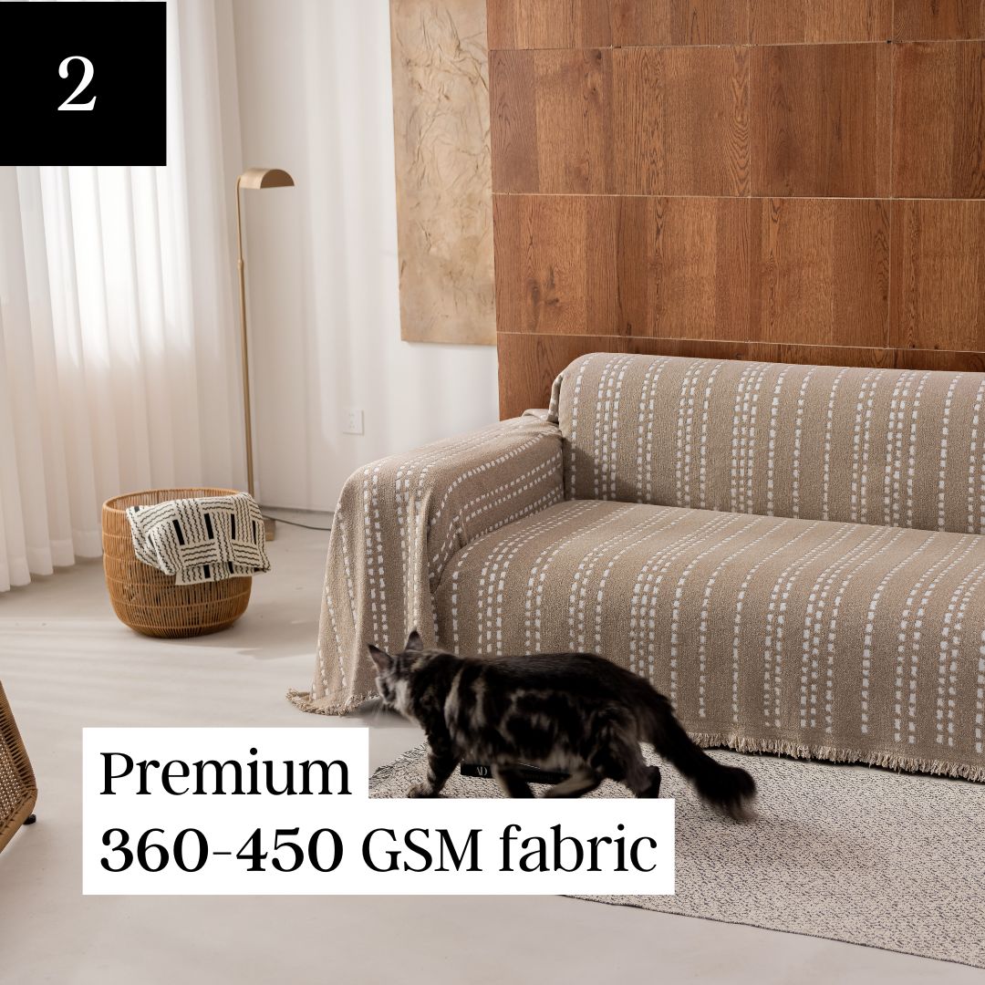 A living room with a patterned couch cover, wooden wall, and a cat walking on the rug.