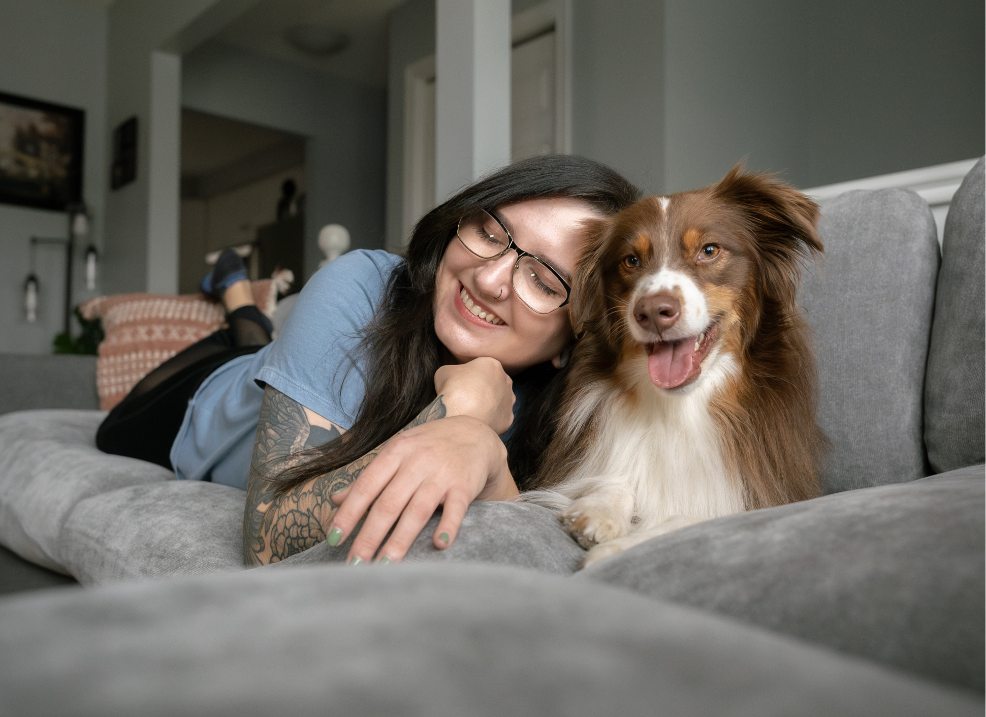 Person smiling with a brown and white dog on a gray couch.
