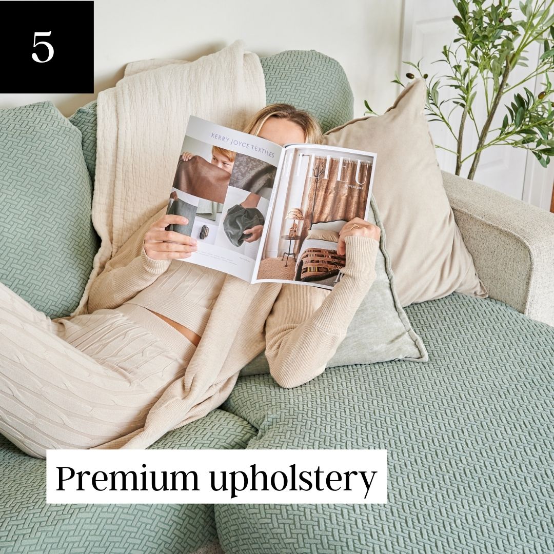 A woman in a cream-colored outfit reads a magazine while lounging on a pale green textured sofa.