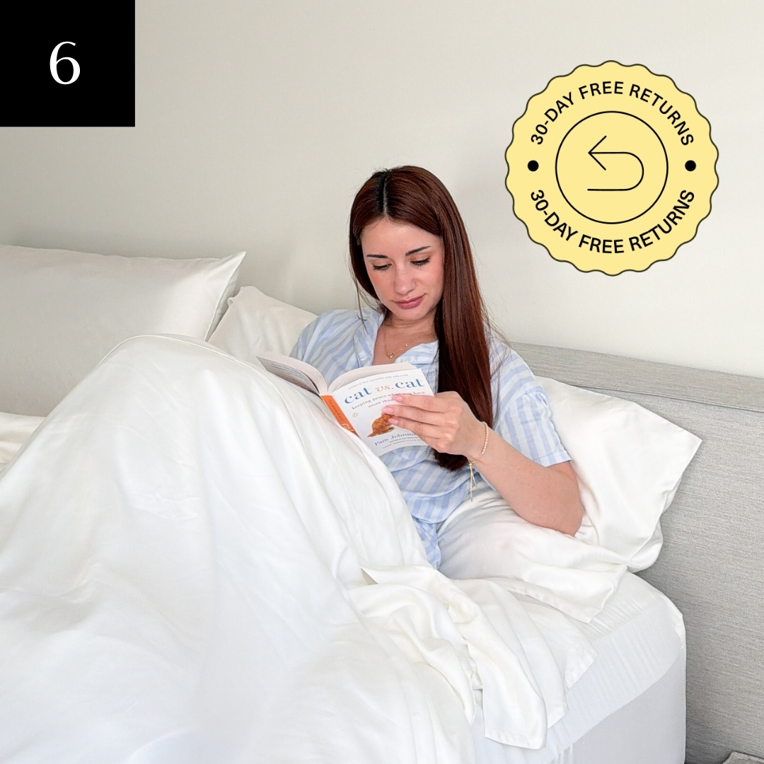 A woman in striped pajamas sits up in a bed with white linens, reading a book.