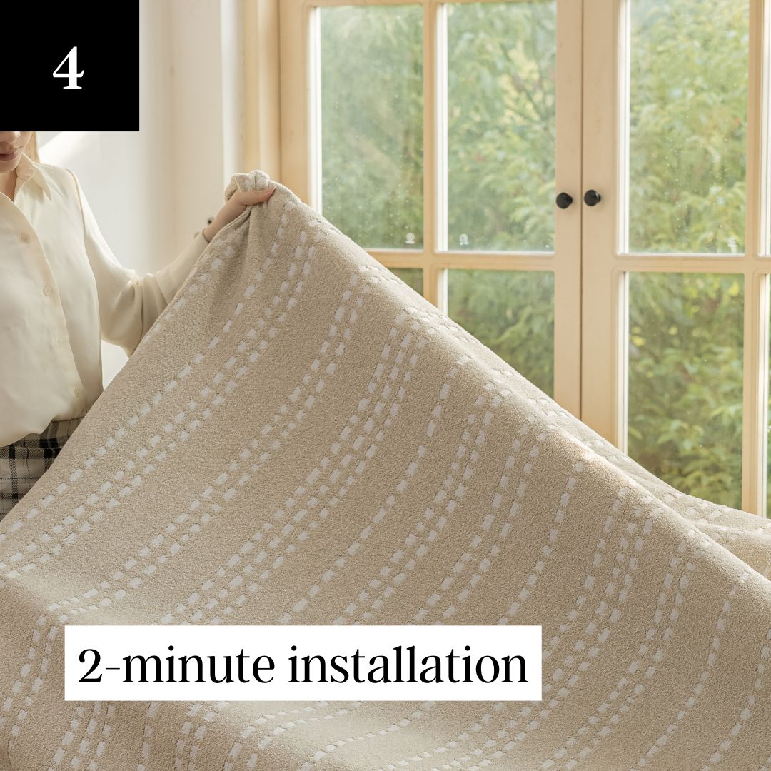 A person drapes a beige, patterned fabric cover over a piece of furniture in front of a window.