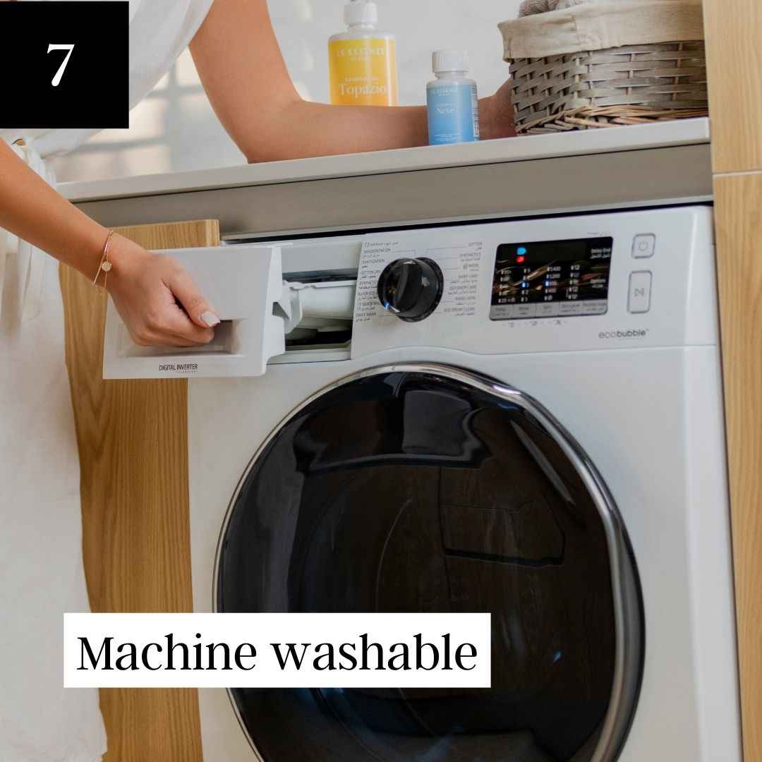A person's hand opens the detergent drawer of a white front-loading washing machine.