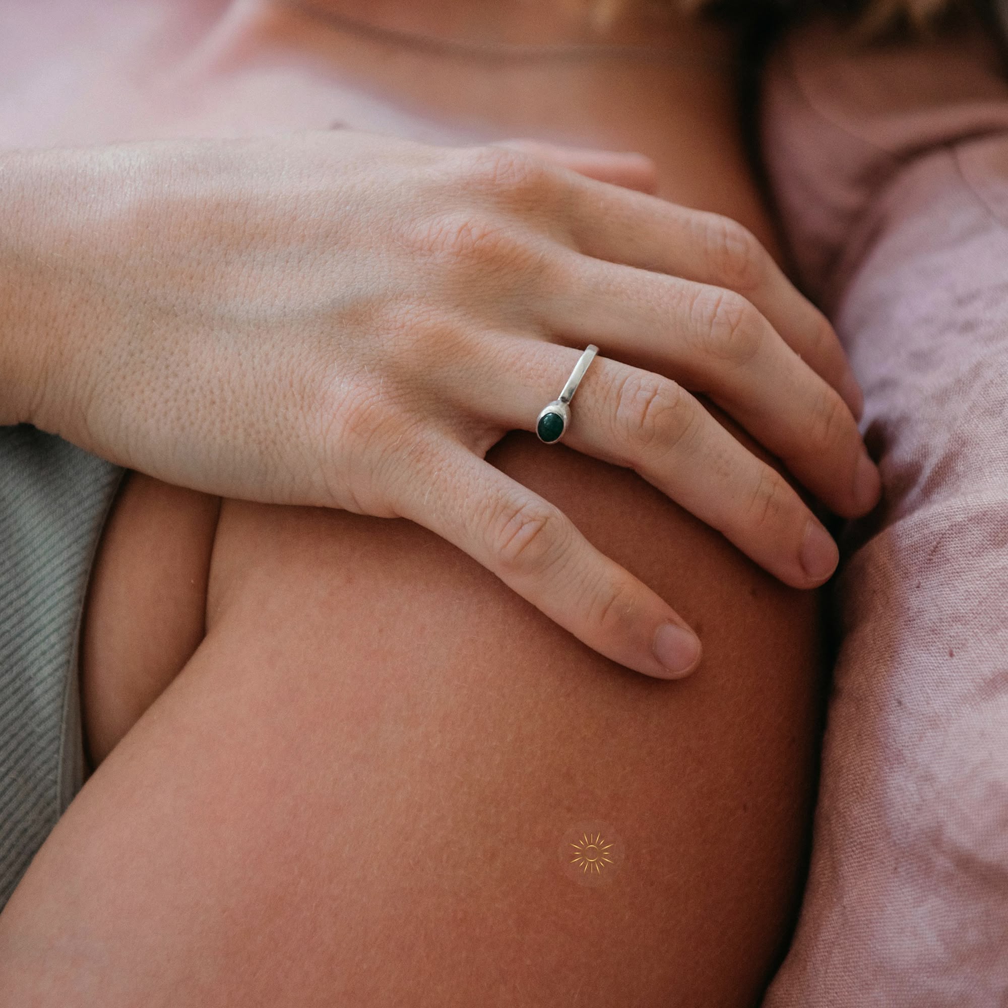 A person's hand with a green-stoned ring resting on a shoulder with a tiny sun sticker.