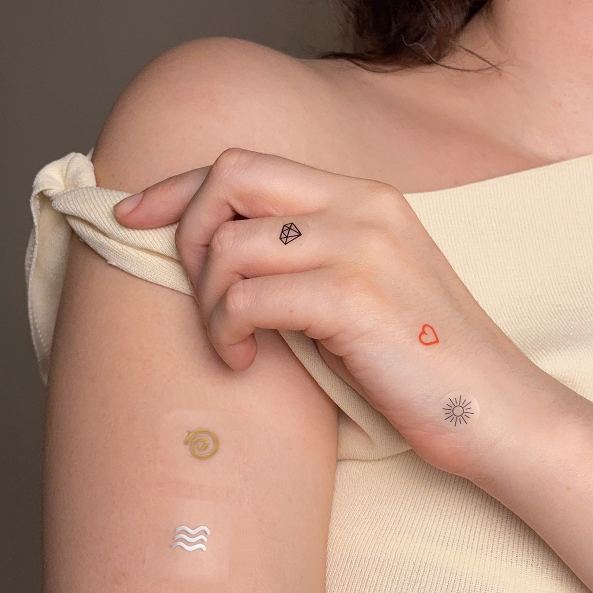 A close-up of a person's arm and hand with several small, temporary tattoos or decorative patches applied.