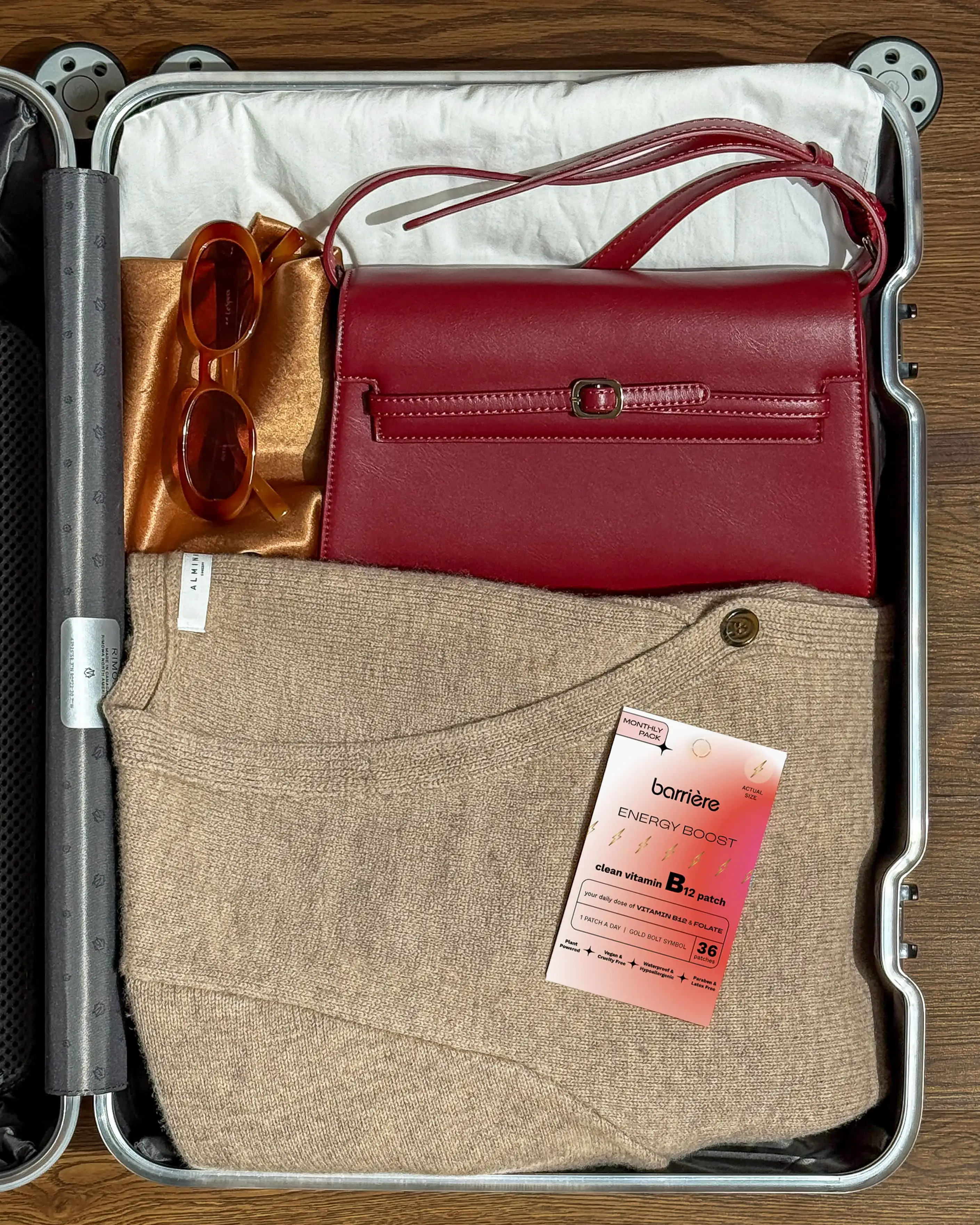 An overhead view of an open suitcase packed with a sweater, red purse, and sunglasses.