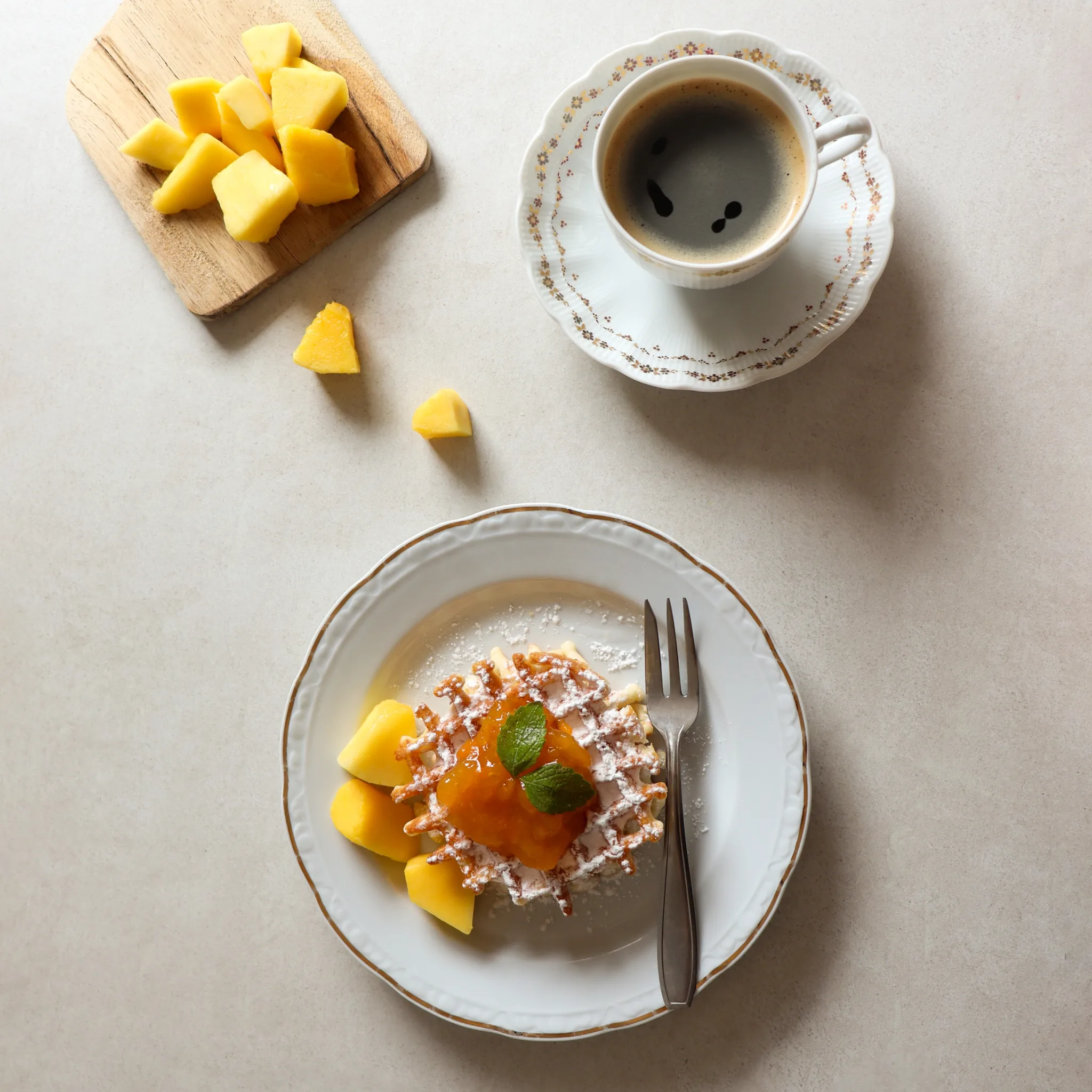 Top-down view of a waffle with jam and mango, served with a cup of black coffee.