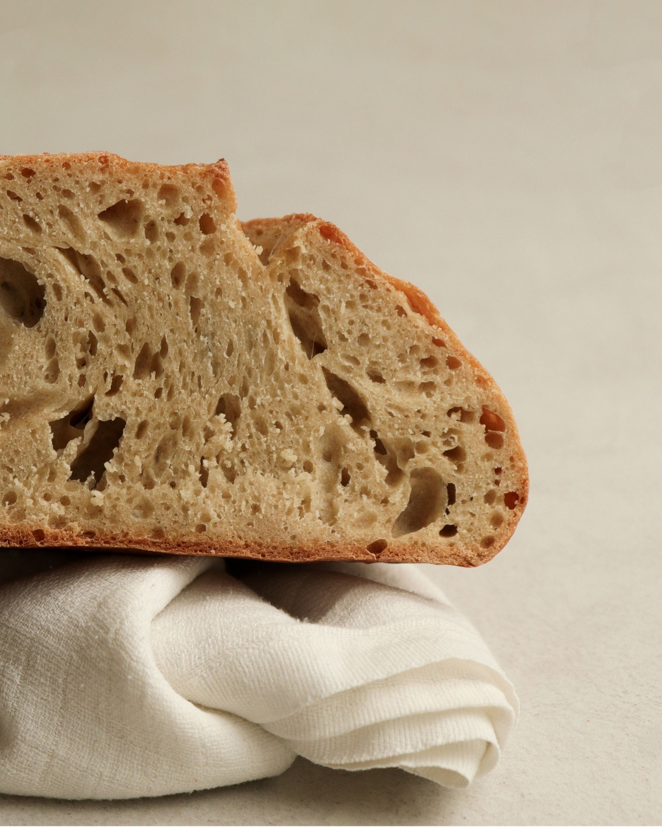 A close-up of a slice of rustic bread with an airy, open crumb, resting on a white cloth.