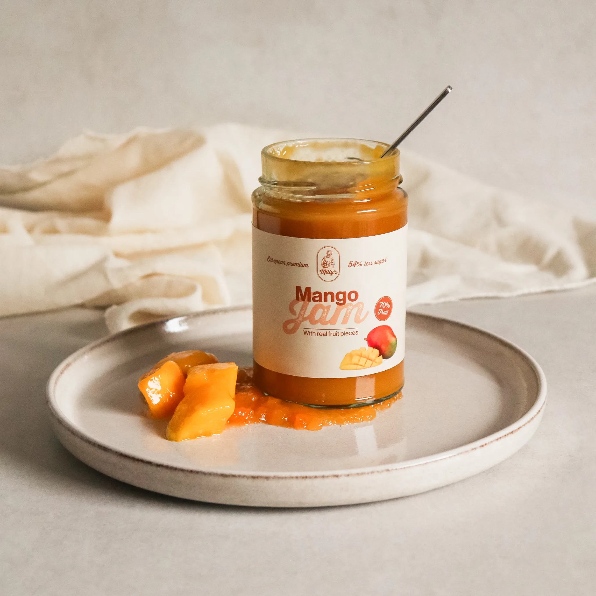 A jar of mango jam sits on a plate with fresh mango pieces and a spoon inside it.