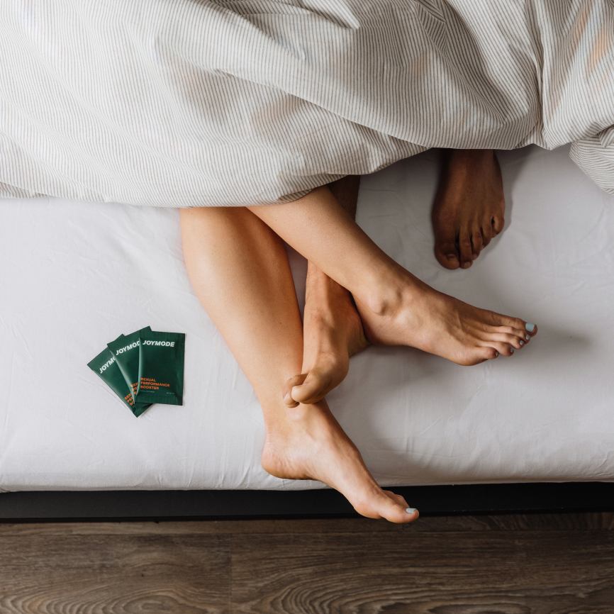 Two pairs of feet intertwined under a striped blanket on a bed.