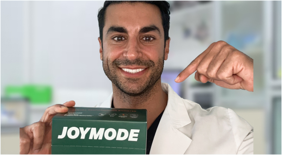 A smiling man in a white coat holds a green box labeled JOYMODE and points toward it.