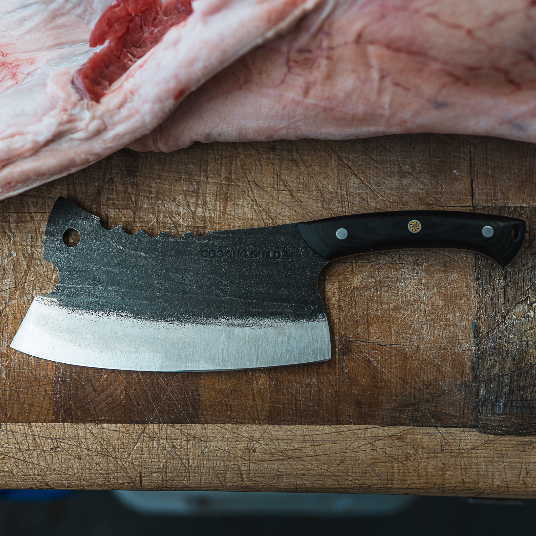 A cleaver on a wooden cutting board next to raw meat.