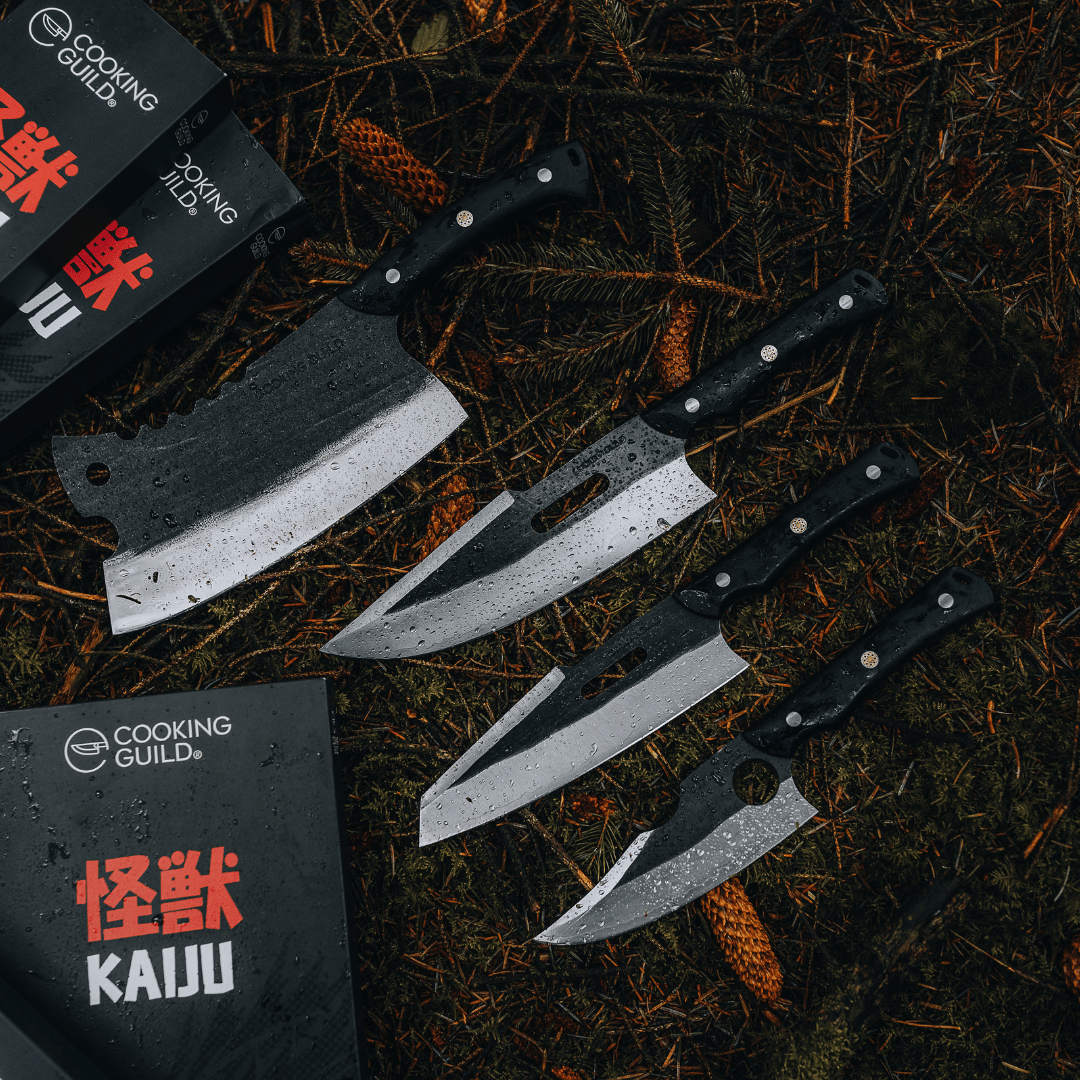 Four knives with black handles on a forest floor, next to Cooking Guild packaging.