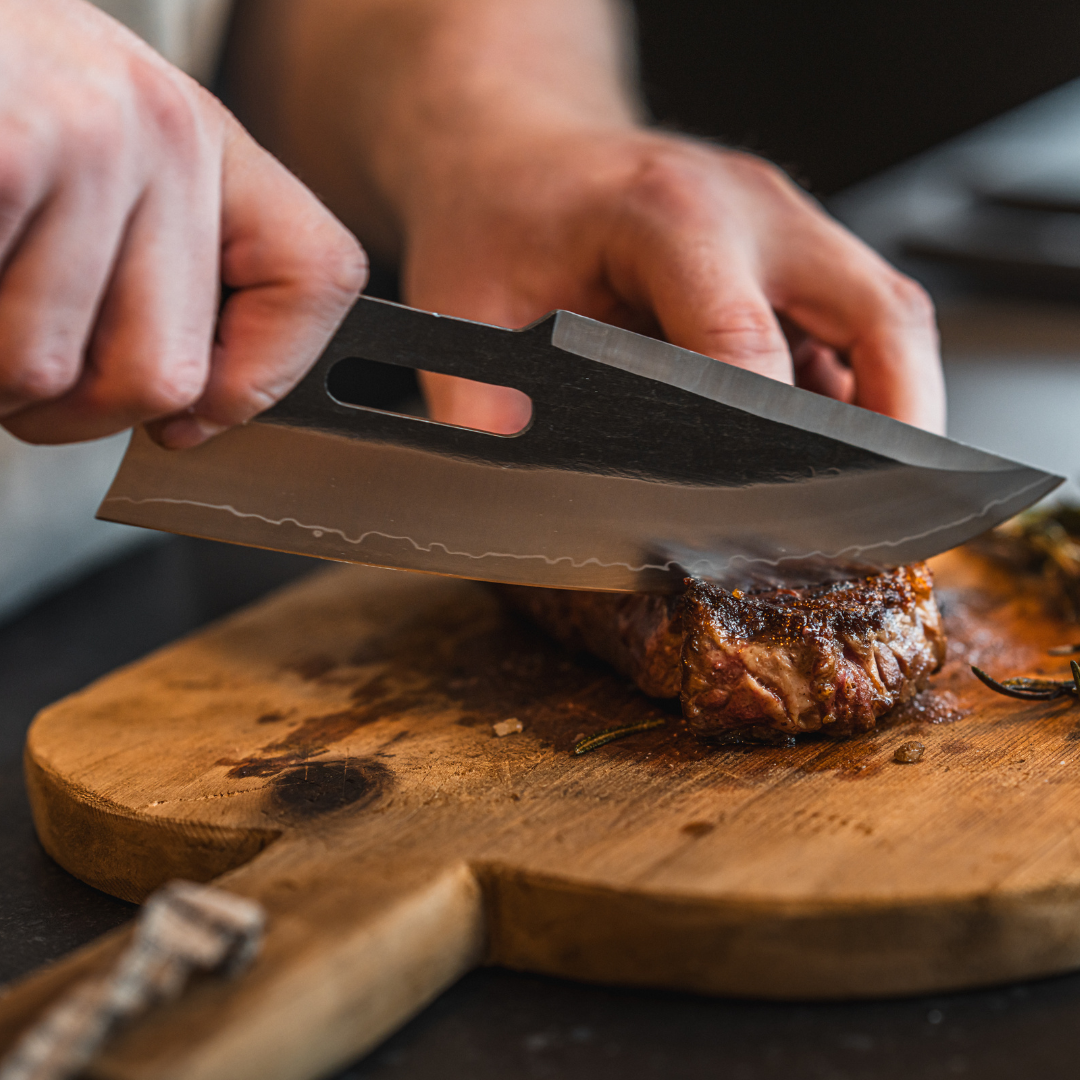 Person slicing cooked meat on a wooden cutting board with a large knife.