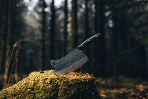 Four knives with black handles stuck in mossy ground in a forest.