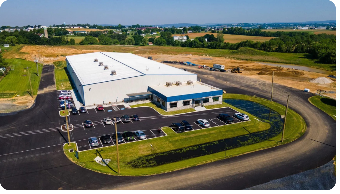 Aerial view of a large industrial building with parking lot and surrounding fields.