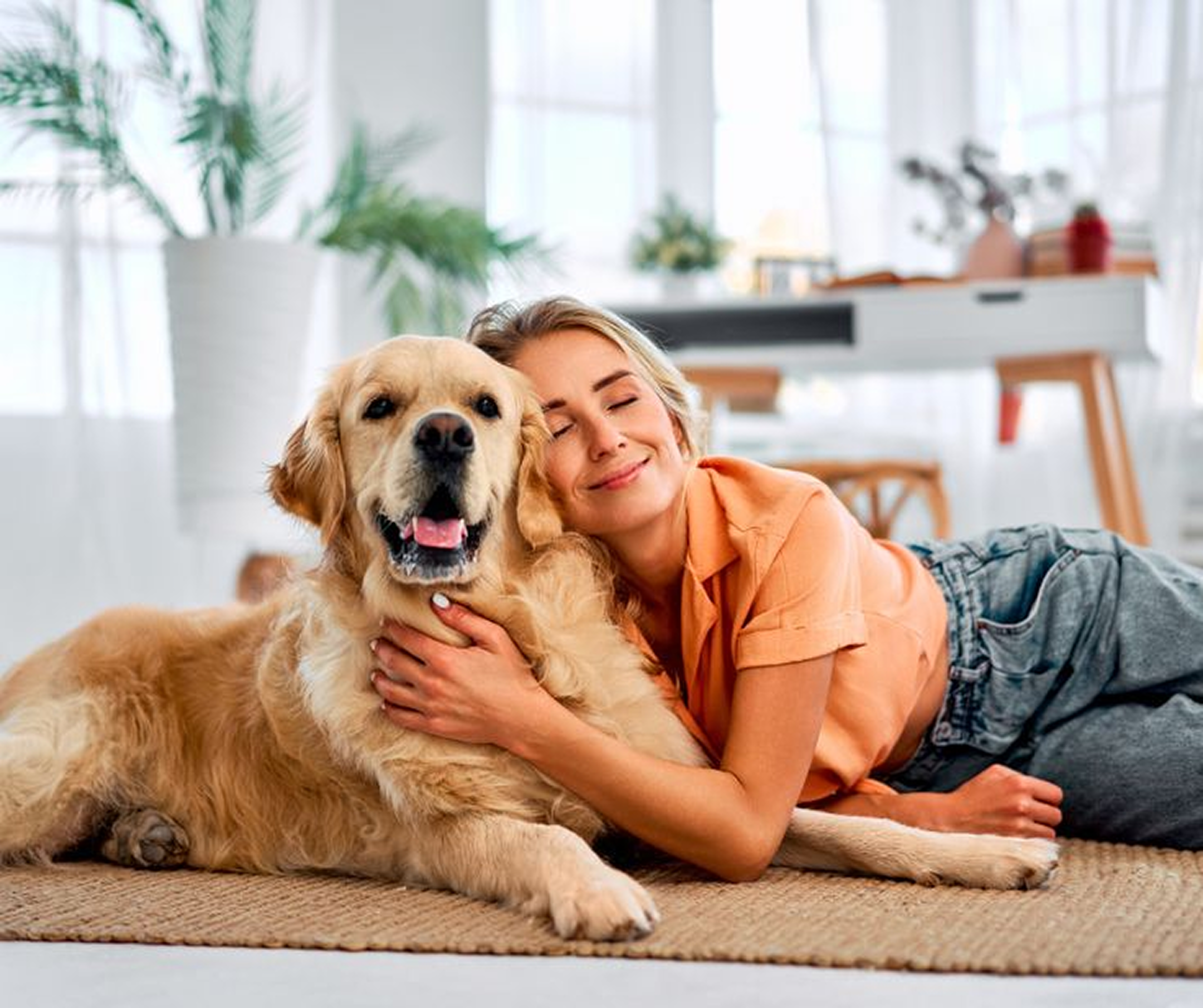 Woman hugging a golden retriever on a rug in a bright room.
