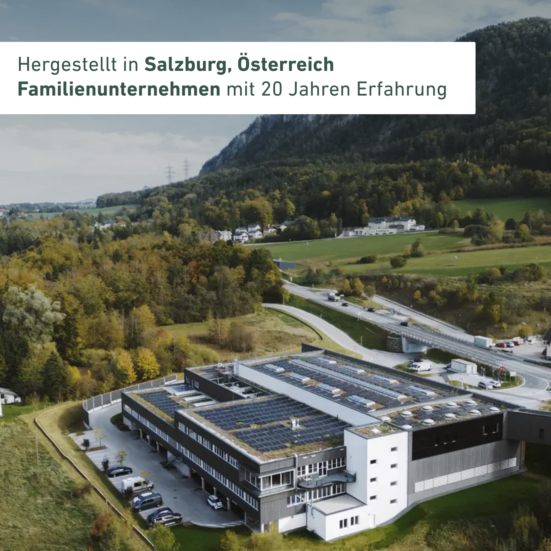 Aerial view of a building with solar panels, surrounded by greenery and mountains.