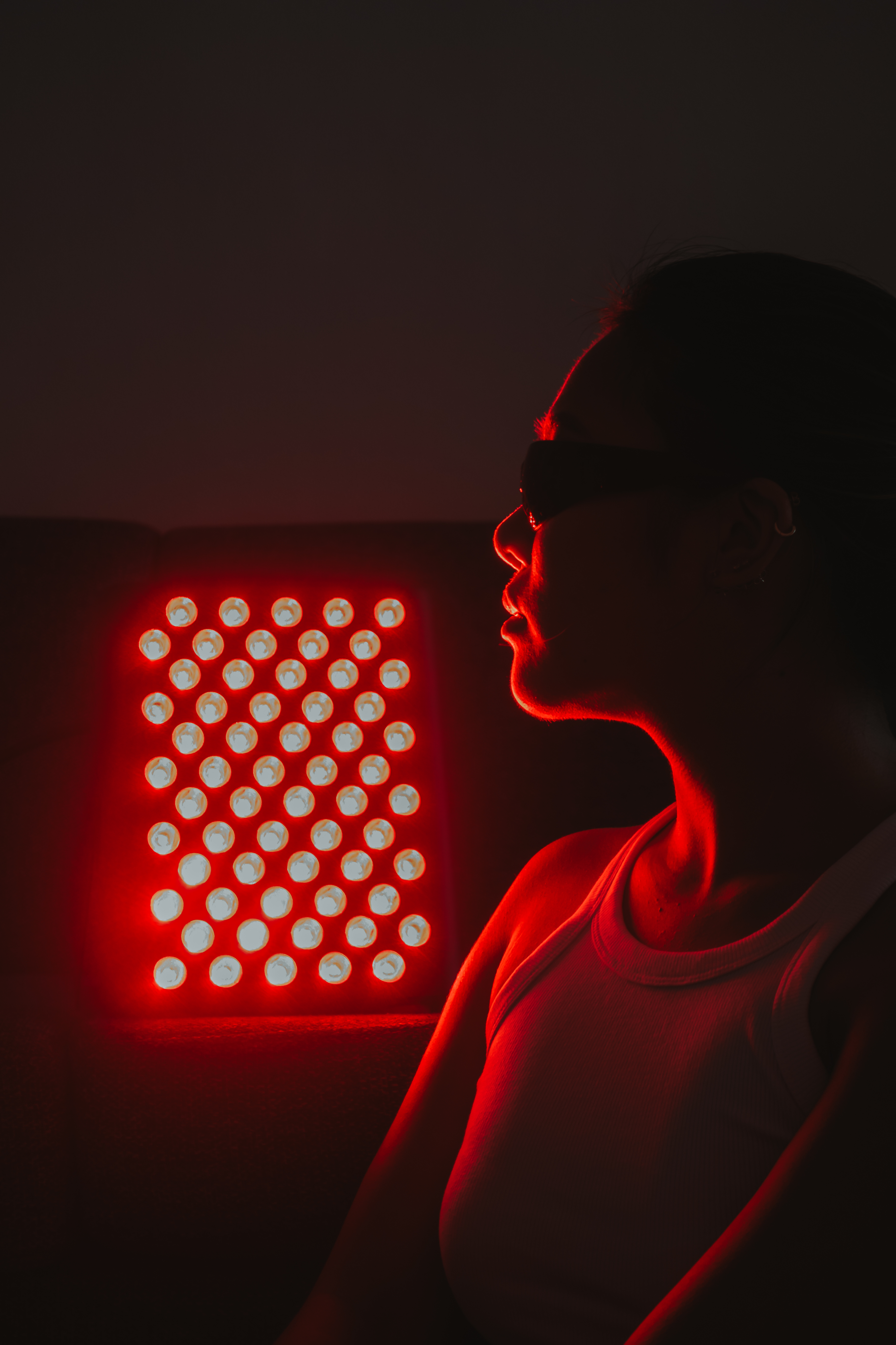 Person wearing sunglasses near a bright red LED light panel.
