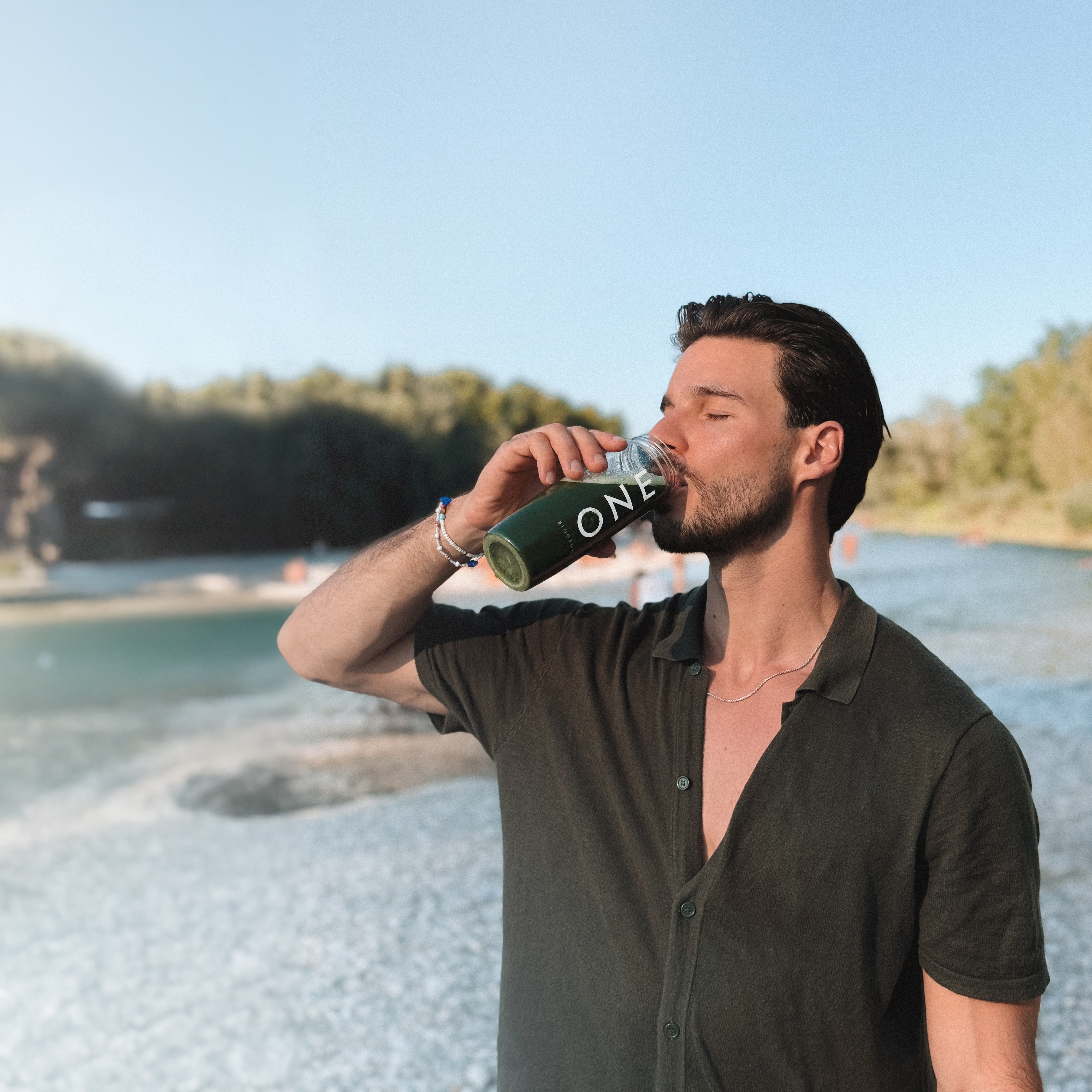 Person drinking from a bottle near a beach.