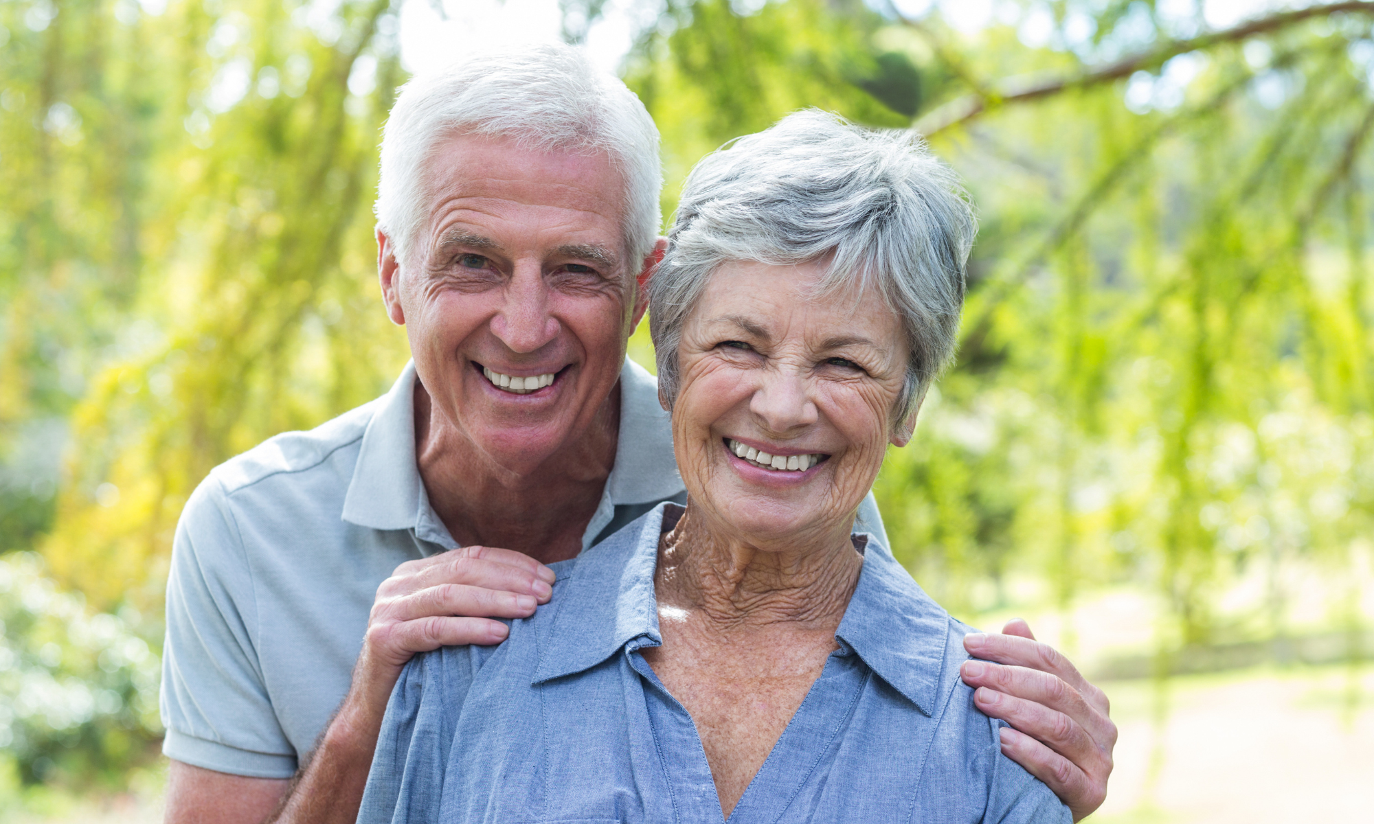 Smiling older couple in a sunny park setting.