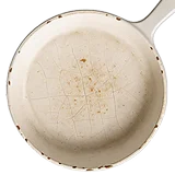 A top-down view of a heavily used, white enameled skillet with a cracked and stained surface.