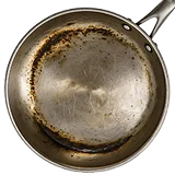 An overhead view of a dirty, stained, and scratched stainless steel frying pan.