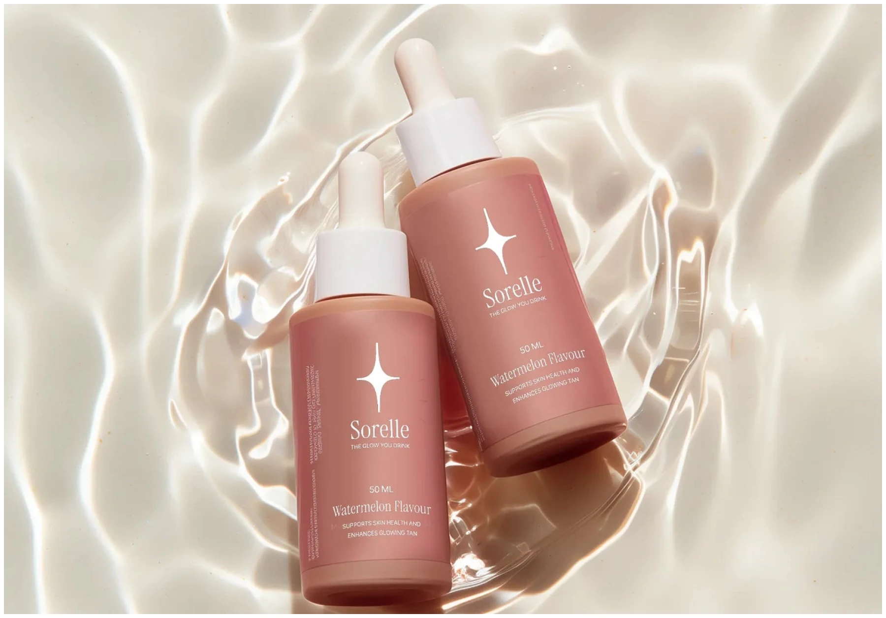 Two pink Sorelle brand dropper bottles lying in clear, rippling water, shot from above.