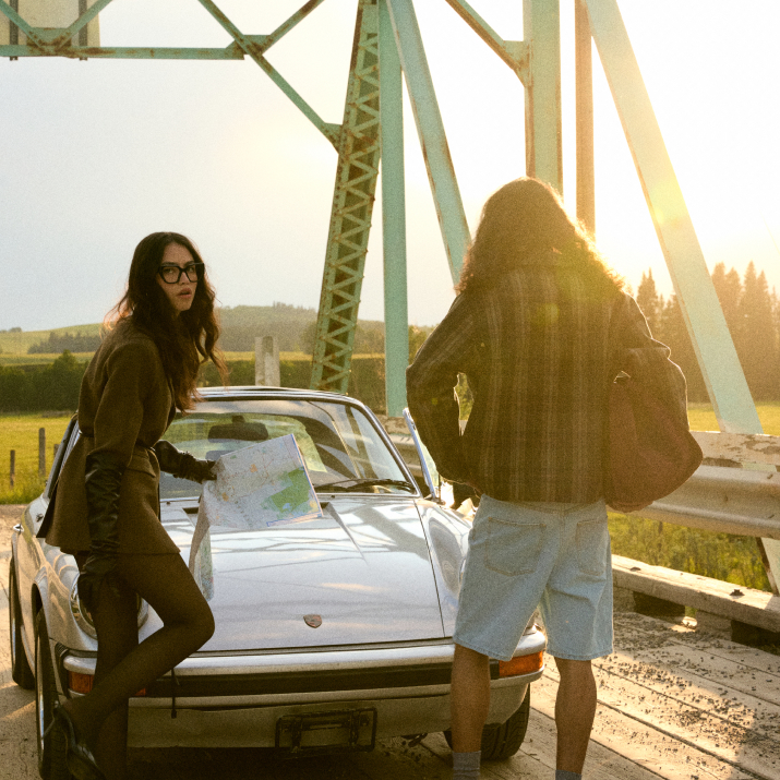 Two people with a map stand by a car on a bridge at sunset.