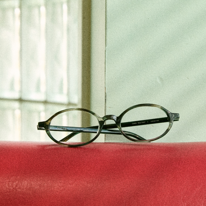 Round eyeglasses resting on a red surface near a window.